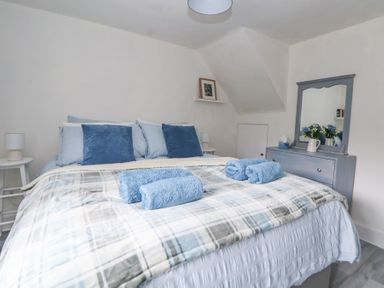 A bedroom with a bed with blue pillows and towels a dresser with a mirror and flowers at Cuddfan at Swallow Cottage in Rhydtalog near Coedpoeth