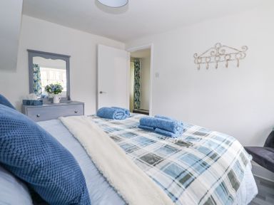 A bedroom with a bed covered in a checkered blanket and blue towels on top a grey dresser with a mirror a door and a wall hook at Cuddfan at Swallow Cottage in Rhydtalog near Coedpoeth