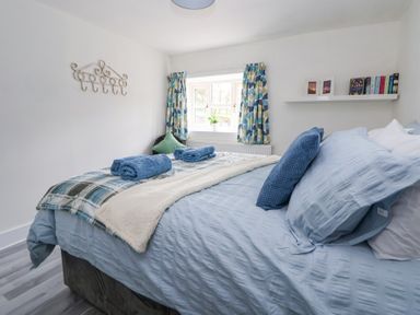 A bedroom with a bed covered in blue bedding two rolled towels on top and a window with patterned curtains at Cuddfan at Swallow Cottage in Rhydtalog near Coedpoeth