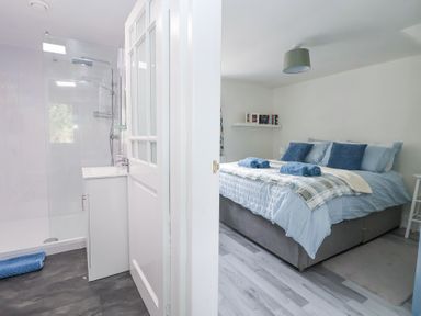 A bedroom with a bed and folded towels next to a bathroom with a shower and sink at Cuddfan at Swallow Cottage in Rhydtalog near Coedpoeth