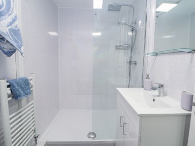 A bathroom with a walk-in shower, white sink cabinet, and blue towels on a rack at Cuddfan at Swallow Cottage Rhydtalog near Coedpoeth