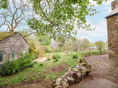 A garden with a wooden shed a fenced patio and trees at Cuddfan at Swallow Cottage in Rhydtalog near Coedpoeth