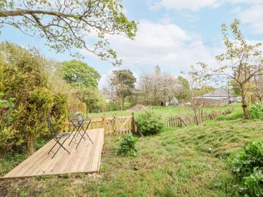A garden with a small wooden deck with table and chairs and a wooden gate at Cuddfan at Swallow Cottage in Rhydtalog near Coedpoeth