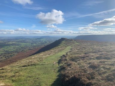 A grassy ridge path leading to hills with a patchwork of fields in the valley below at White Haywood Farmhouse & Barn in Craswall