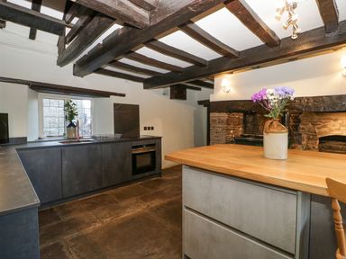 A kitchen with dark cabinets a wooden countertop flowers in a vase and a window with wooden beams on the ceiling at White Haywood Farmhouse & Barn in Craswall