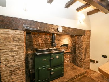 A rustic kitchen corner with a green cast iron stove set in a stone fireplace at White Haywood Farmhouse & Barn in Craswall