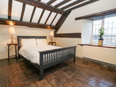 A bedroom with a double bed, two bedside tables with lamps, exposed wooden beams and a window with a vase of flowers at White Haywood Farmhouse & Barn in Craswall
