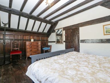 A bedroom with wooden beams a bed a chest of drawers two chairs and a mirror at White Haywood Farmhouse & Barn in Craswall