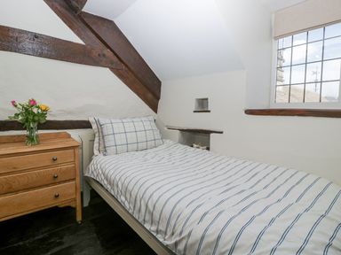 A bedroom with a single bed with striped bedding a wooden chest of drawers with a vase of flowers and a window at White Haywood Farmhouse & Barn in Craswall
