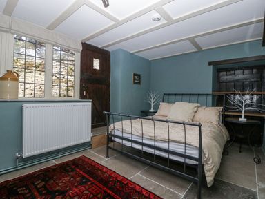A bedroom with a metal bed frame beige bedding two side tables with decorative trees a window and a wooden door at White Haywood Farmhouse & Barn in Craswall