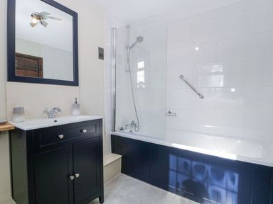 A bathroom with a black vanity, mirror, bathtub with shower and glass screen at White Haywood Farmhouse & Barn Craswall