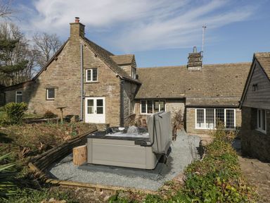 An outdoor hot tub with bubbling water in a garden area next to a stone house at White Haywood Farmhouse & Barn in Craswall