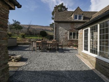 A courtyard with a wooden dining table and chairs outside a stone house at White Haywood Farmhouse & Barn in Craswall