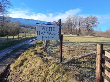 A farm sign on a post next to a dirt road and fenced grassy field at White Haywood Farmhouse & Barn in Craswall