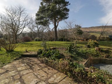 A garden with grass trees shrubs and a paved stone pathway at White Haywood Farmhouse & Barn in Craswall