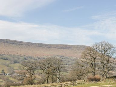 A rural landscape with trees, a fence, and hills in the background at White Haywood Farmhouse & Barn in Craswall