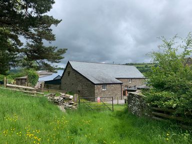 A stone farmhouse with a slate roof surrounded by green grass and trees at White Haywood Farmhouse & Barn in Craswall