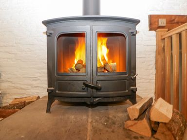 A wood-burning stove with fire inside and a pile of firewood next to it at White Haywood Farmhouse & Barn in Craswall