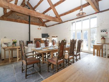 A dining area with wooden table and chairs near a sitting area with white sofas and a fireplace at White Haywood Farmhouse & Barn in Craswall