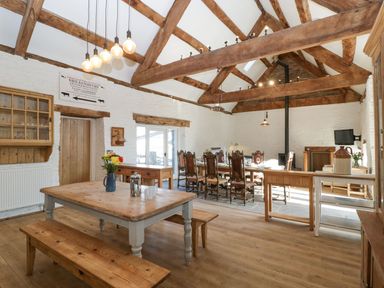 A dining room with wooden tables benches and chairs and exposed wooden beams at White Haywood Farmhouse & Barn in Craswall