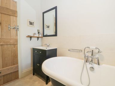 A bathroom with a bathtub and a black vanity with a mirror above at White Haywood Farmhouse & Barn in Craswall