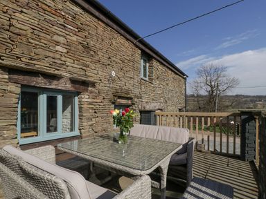 An outdoor seating area with a glass table and wicker chairs on a wooden deck outside a stone building at White Haywood Farmhouse & Barn in Craswall