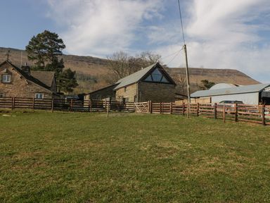A fenced grassy area with stone buildings and hills in the background at White Haywood Farmhouse & Barn in Craswall
