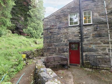 An outdoor area with a stone wall and seating at Sygun Cottage Nant Gwynant