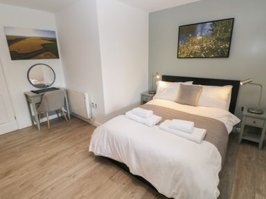 A bedroom with a double bed white linens bedside tables with lamps a desk with a round mirror and a chair at Sycamore in Cowbridge