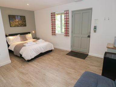 A bedroom with a bed folded towels a window with plaid curtains a door and wooden flooring at Sycamore in Cowbridge