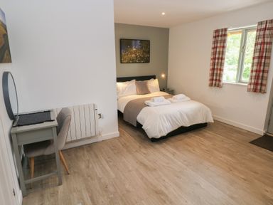 A bedroom with a double bed bedside table a desk chair window and curtains at Sycamore in Cowbridge