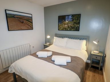 A bedroom with a double bed two bedside tables with lamps and framed pictures on the walls at Beech in Cowbridge