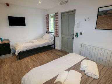 A room with two beds a wall-mounted TV a wooden floor and a door at Beech in Cowbridge