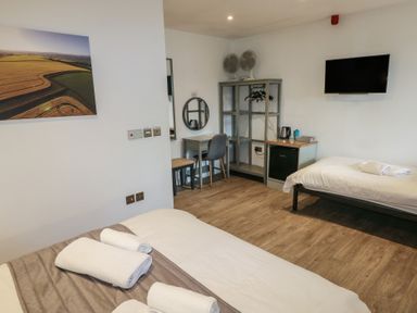 A bedroom with two single beds a desk a chair a small fridge shelves and a wall-mounted TV at Beech in Cowbridge