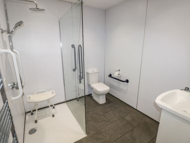 A bathroom with a walk-in shower with a shower chair a toilet with a grab bar and a sink at Beech in Cowbridge