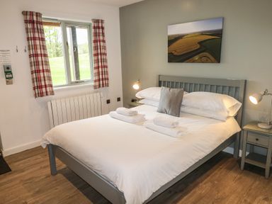 A bedroom with a double bed white bedding bedside tables and lamps a window with check curtains and a landscape picture on the wall at Alder in Cowbridge
