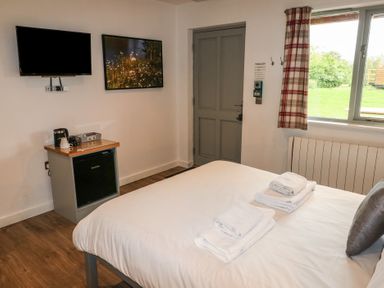A bedroom with a bed towels a small fridge a television a picture on the wall and a window with curtain at Alder in Cowbridge