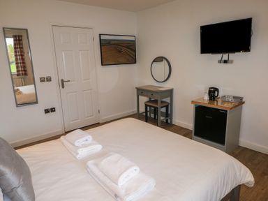 A bedroom with a bed towels a mirror a desk a chair a mini fridge a kettle and a wall-mounted television at Alder in Cowbridge