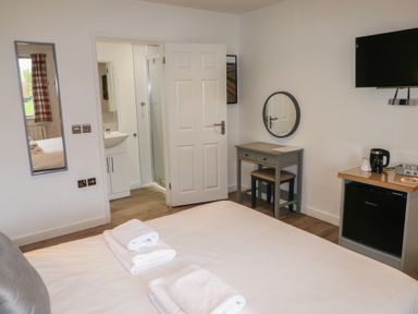 A bedroom with a bed towel stacks a wall mirror a small desk with a round mirror a television and a mini fridge at Alder in Cowbridge