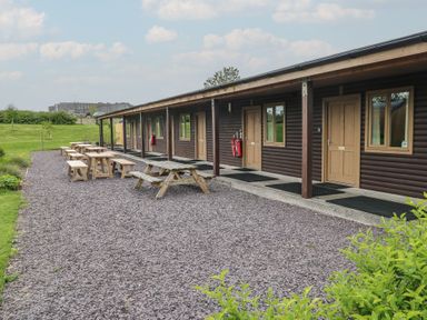 An outdoor area with wooden picnic tables and benches next to a building with multiple doors and windows at Cherry in Cowbridge