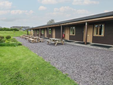 A row of wooden cabins with picnic tables outside on gravel at Chestnut in Cowbridge