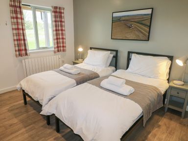A bedroom with two single beds with white bedding and towels on them bedside tables with lamps and a window with plaid curtains at Oak in Cowbridge