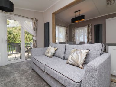 A living room with a grey sofa and patterned cushions next to glass doors leading to a balcony at 16 Manleigh Park in Combe Martin