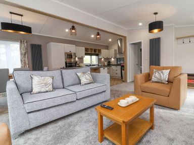A living room with a gray sofa, brown armchair, wooden coffee table, and kitchen in the background at 16 Manleigh Park in Combe Martin