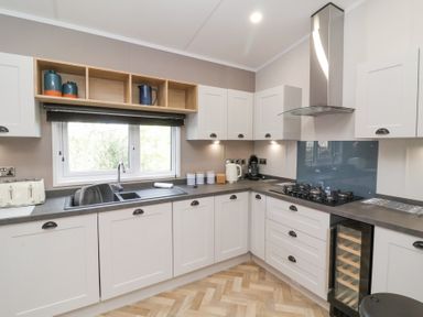 A kitchen with white cabinets a gas stove a sink and a wine cooler at 16 Manleigh Park in Combe Martin