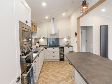 A kitchen with white cabinets and a countertop with stools at 16 Manleigh Park in Combe Martin