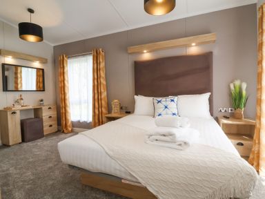 A bedroom with a bed, desk, mirror, and curtains at 16 Manleigh Park in Combe Martin