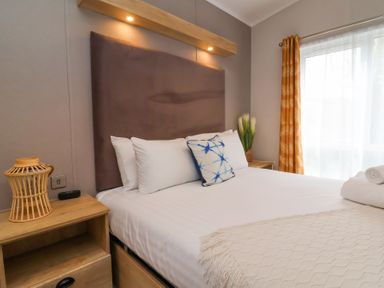 A bedroom with a bed with white and blue pillows bedside tables and windows with curtains at 16 Manleigh Park in Combe Martin
