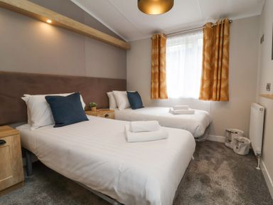 A bedroom with two single beds white bedding blue pillows wooden nightstands and orange curtains at 16 Manleigh Park in Combe Martin