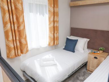 A small bedroom with a single bed a bedside table with a plant and books and a window with yellow curtains at 16 Manleigh Park Combe Martin